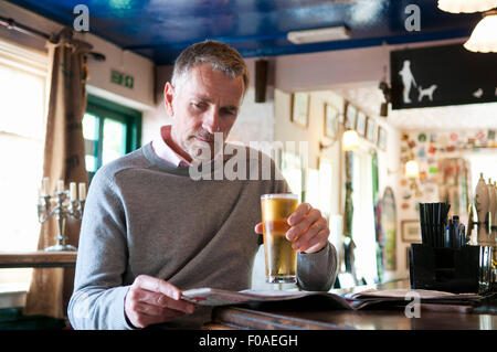 Reifer Mann trinkt Bier und liest Zeitung im pub Stockfoto