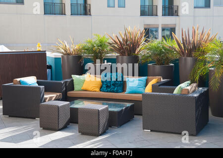 Stilvolle moderne Rattan Gartenmöbel in dunkelbraun mit bunten Kissen in einem Sitzbereich umgeben von Topfpflanzen Stockfoto