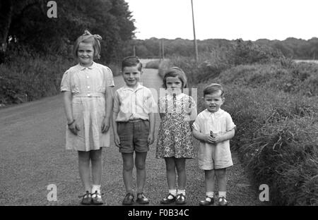 Vier kleine Kinder stehen in der Reihenfolge der Höhe auf einer Landstraße. Stockfoto