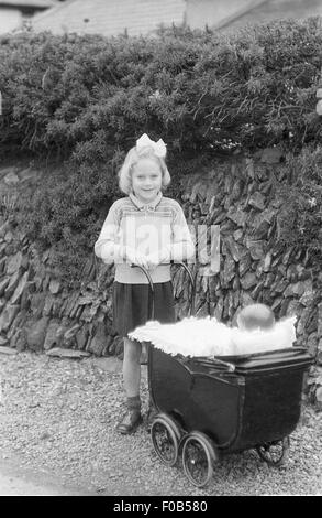 Ein junges Mädchen mit ihren Puppen Kinderwagen im Garten Stockfoto