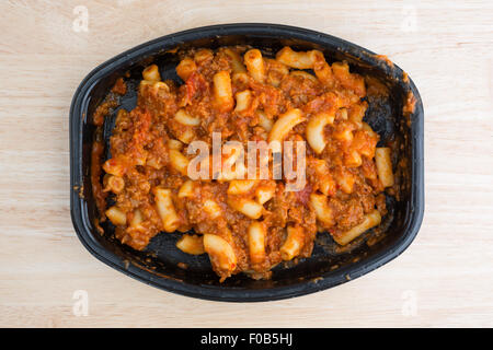 Draufsicht auf eine Mikrowelle Rindfleisch und Makkaroni TV Dinner in einer schwarzen Schale auf einer hölzernen Tischplatte mit natürlichen Fensterlicht beleuchtet. Stockfoto