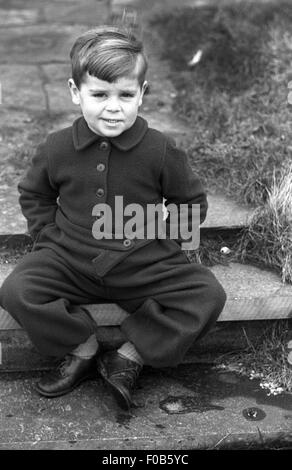 Ein kleiner Junge mit einem Seitenscheitel tragen ein All-in - einem wollenen Hosenanzug auf Schritte im Garten. Stockfoto