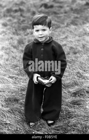 Ein kleiner Junge mit einem Seitenscheitel tragen ein All-in - einem wollenen Hosenanzug stehen im Garten. Stockfoto