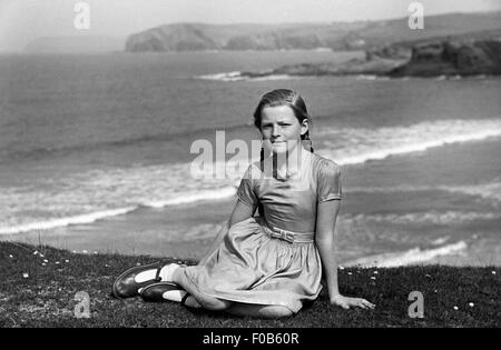 Mädchen Kleid sitzt am Rand der Klippe mit dem Meer im Hintergrund Stockfoto