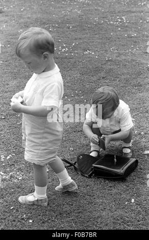 Zwei jungen auf der Suche auf den Inhalt von einer Frau die Handtasche auf dem Rasen im Garten. Stockfoto