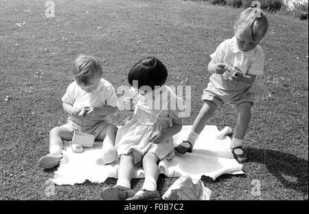 Zwei jungen und ein Mädchen spielen auf einer Decke in einem Garten im Sommer. Stockfoto