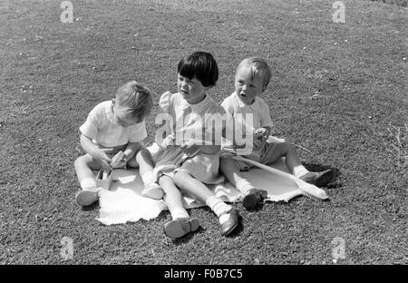 Zwei jungen und ein Mädchen spielen auf einer Decke in einem Garten im Sommer. Stockfoto