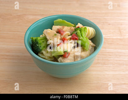 Eine kleine Schüssel mit einer Portion mit gegrilltem Hähnchen Stücke und verschiedene Gemüse in einer Knoblauchsauce auf einer hölzernen Tischplatte Stockfoto