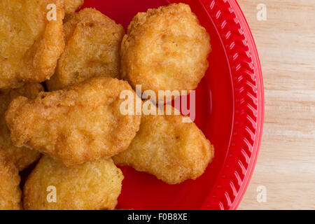 Enge Draufsicht einer Portion Hähnchen-Nuggets auf einer roten Platte auf einer hölzernen Tischplatte mit Fensterlicht beleuchtet. Stockfoto