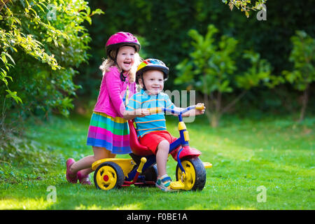 Kinder Reiten Fahrräder in einem Park. Kinder Fahrrad Fahrt im Garten genießen. Mädchen auf einem Fahrrad und kleiner Junge auf einem Dreirad Stockfoto
