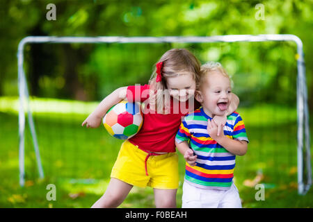 Zwei glückliche Kinder spielen Fußball im Freien im Schulhof. Kinder spielen Fußball. Aktiv Sport für Vorschulkind. Stockfoto