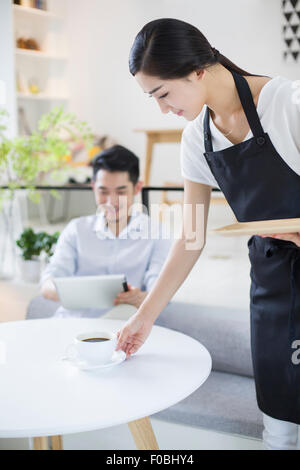 Kellnerin serviert junge Mann eine Tasse Kaffee Stockfoto