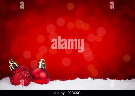 Zwei kleine rote Christbaumkugeln auf Schnee mit defokussierten roten Lichtern im Hintergrund. Stockfoto