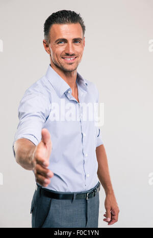 Porträt eines glücklichen Geschäftsmann stretching Hand für Handshake auf grauem Hintergrund Stockfoto