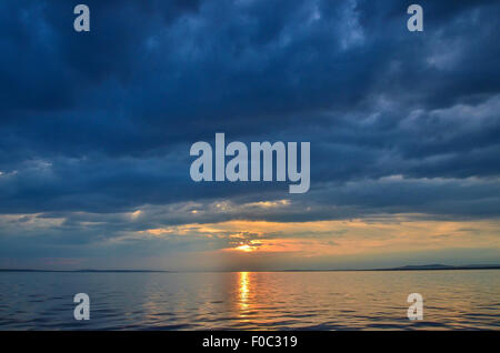 Ein Sonnenuntergang über dem Bodensee mit der Küste in der Ferne, dunkle Wolken und plätschernden Wellen Stockfoto