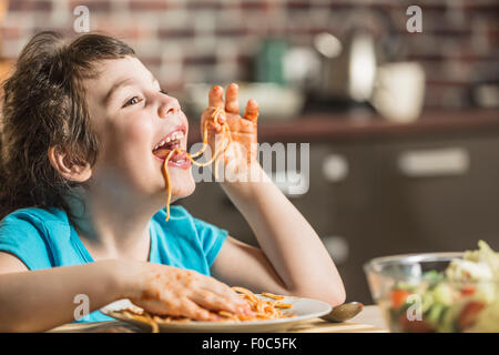 Fröhliches kleines Mädchen zu Hause essen Spaghetti mit Händen Stockfoto