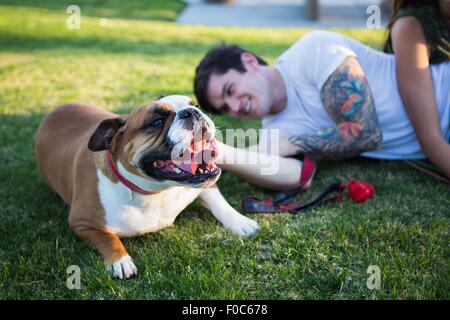 Junger Mann im Park Petting Bulldogge liegend Stockfoto