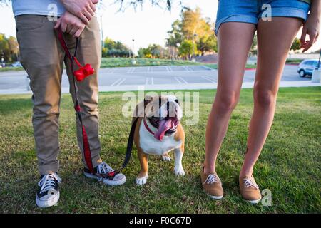 Porträt der Bulldogge im Park zwischen den Beinen des jungen Paares Stockfoto