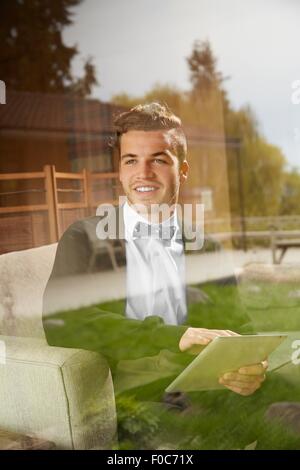 Erschossen Sie durch Fenster der Mann sitzt auf dem Sofa mit digital-Tablette Stockfoto