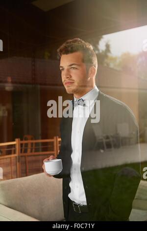 Fenster der Mann auf der ständigen Suche durchzuckte heraus den Blick halten Tasse Kaffee Stockfoto