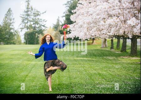 Porträt der jungen Frau, Yoga zu praktizieren, während Sie Blumenstrauß im Park zu halten Stockfoto