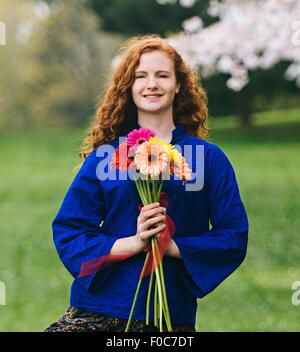 Porträt der jungen Frau mit lange gewellte rote Haare halten Blumenstrauß im park Stockfoto
