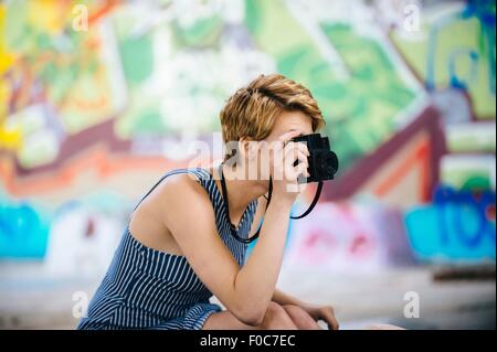 Stilvolle Teenager-Mädchen fotografieren mit der Kamera vor Graffitiwand Stockfoto