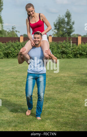 Gesamte Länge der glückliche junge Mann trägt Frau auf Schultern im Hinterhof Stockfoto