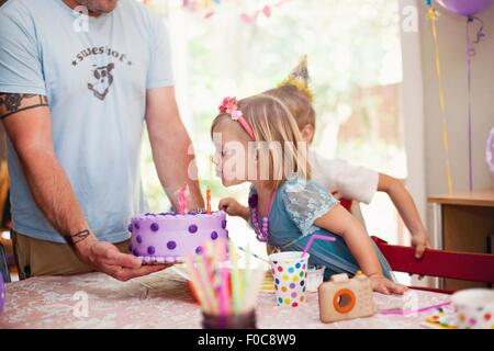 Porträt von blonden Mädchen Ausblasen der Kerzen auf lila Kuchen Stockfoto