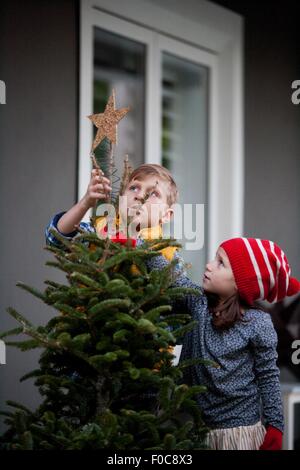 Porträt eines jungen und Mädchen setzen Sterne Dekoration auf Weihnachtsbaum Stockfoto