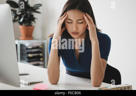 Junge Geschäftsfrau, leiden unter Kopfschmerzen am Schreibtisch im Büro Stockfoto