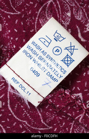 Pflegehinweise Etikett in rot gemustertem Kleid - Pflege waschen Symbole und Anweisungen Stockfoto