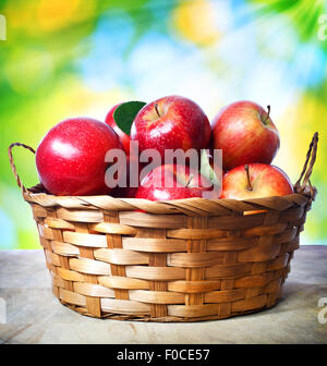 Frische Äpfel im Korb über glänzende Blätter Hintergrund Stockfoto