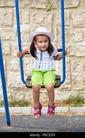 Babymädchen auf einer Schaukel. Kind in einem weißen Hut, draußen zu spielen. Stockfoto