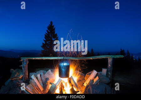 Kochen in den Topf auf dem Feuer unter blauen Nachthimmel mit vielen stars Stockfoto