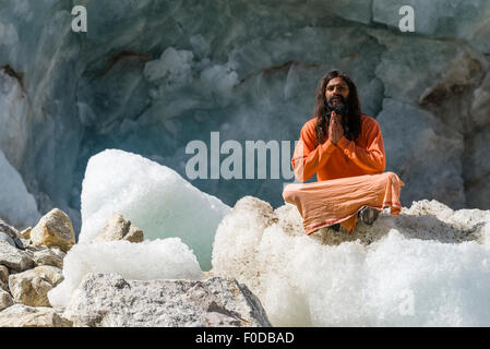 Ein Sadhu, heiliger Mann, sitzt und in Lotus Pose, Padmasana, auf einem Eisblock am Gaumukh, die wichtigste Quelle des Heiligen Geistes zu beten Stockfoto
