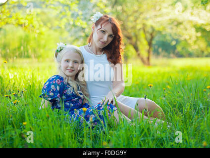 Entzückende glückliches Babymädchen mit Mutter in einen wunderschönen blühenden Obstgarten mit weißen Blüten auf Apfelbäume Stockfoto