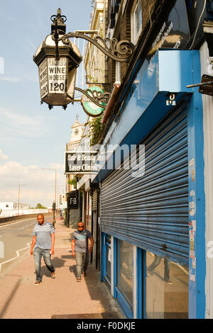 Zwei schwarze Männer Fuß vorbei an heruntergekommenen Weinbar in Woolwich Hight Street in London SE18 Stockfoto