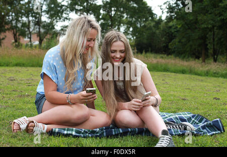 Zwei Mädchen im Teenageralter im Freien mit Blick auf ihren Handys Stockfoto