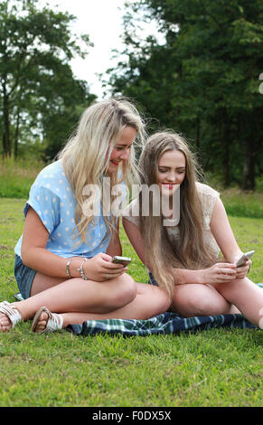 Zwei Mädchen im Teenageralter im Freien mit Blick auf ihren Handys Stockfoto