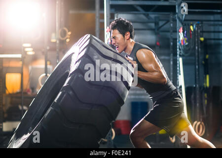 Junger Mann drängen große Reifen in Crossfit gym Stockfoto