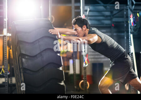 Junger Mann drängen große Reifen in Crossfit gym Stockfoto