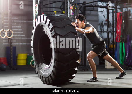 Junger Mann drängen große Reifen in Crossfit gym Stockfoto