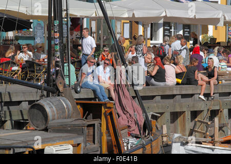 Leute treffen und reden, um sich bei einem Drink in der Sonne auf dem Kai im gemütlichen Ambiente in bezaubernden Nyhavn. Viele bevorzugen auf der Werft unter den alten Schiffen zu sitzen. Hygge. Stockfoto