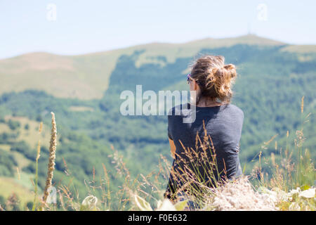 Junge Frau mit Rucksack sitzt am Rande der Klippen und mit Blick auf Berge und klarer Himmel. Sommer Wandern Reise-Abenteuer Stockfoto