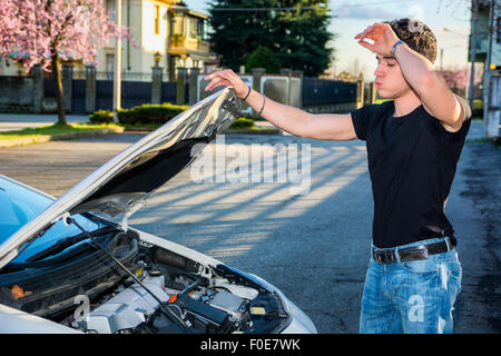 Hübscher junger Mann versucht, einen Automotor, reparieren Blick in offene Motorhaube Stockfoto