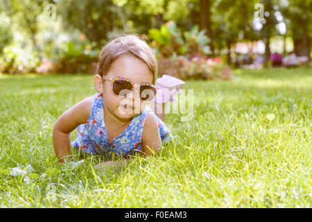 Niedliche kleine Mädchen mit Brille, die Verlegung in den Rasen an einem sonnigen Sommertag Stockfoto