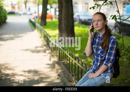 Teenager-Mädchen sehnsüchtig auf dem Handy beim Sitzen im freien sprechen. Stockfoto