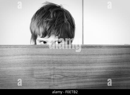 Angst vor kleinen Mädchen versteckt. Sie verbirgt sich hinter einer Holzoberfläche spähen mit einem besorgten Blick auf ihrem Gesicht. Stockfoto