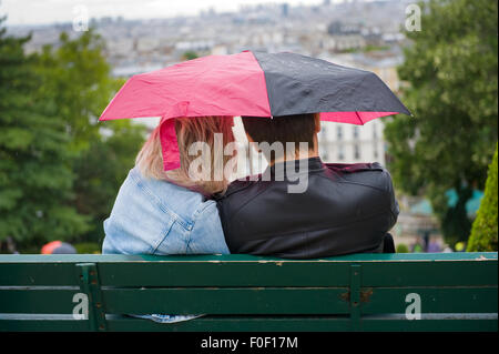 PARIS, Frankreich - 27. Juli 2015: Ein paar auf einer Bank unter einem Dach in einem regnerischen Tag in Mont Matre in Paris in Fra sitzt Stockfoto